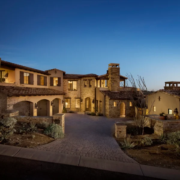Twilight view of a stone and stucco townhouse complex with warm-lit windows and tall cacti in the foreground.