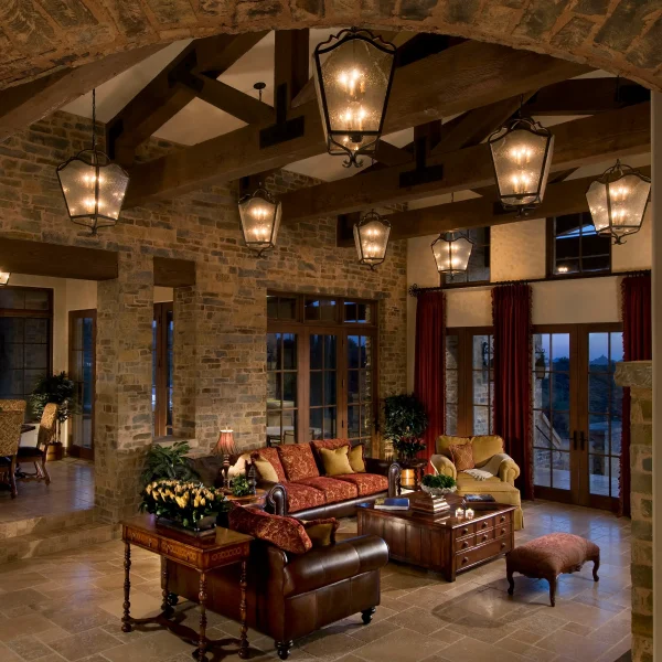 Luxurious lodge‑style living room with stone walls, exposed wooden beams, and multiple lit lantern chandeliers.